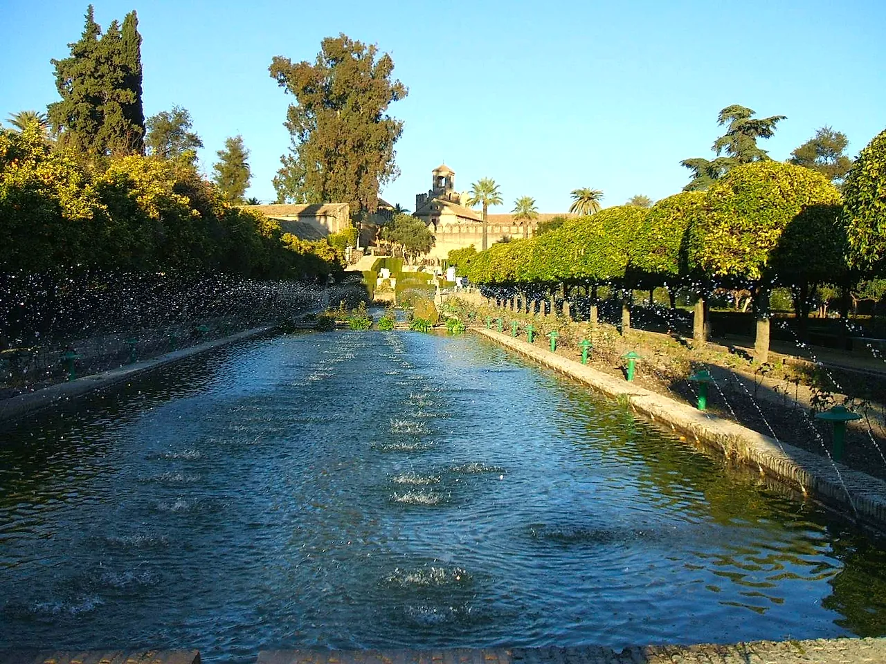 The long pond with water jets in the gardens of the Alcázar de los Reyes Cristianos, lined with trees and trimmed hedges