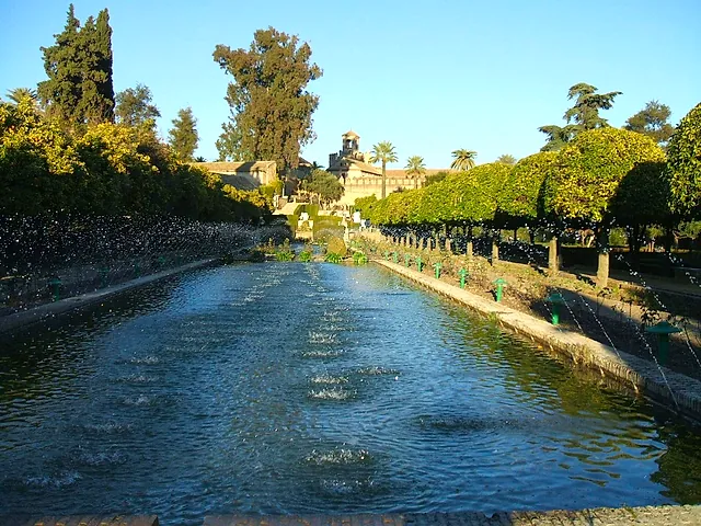 The long pond with water jets in the gardens of the Alcázar de los Reyes Cristianos, lined with trees and trimmed hedges