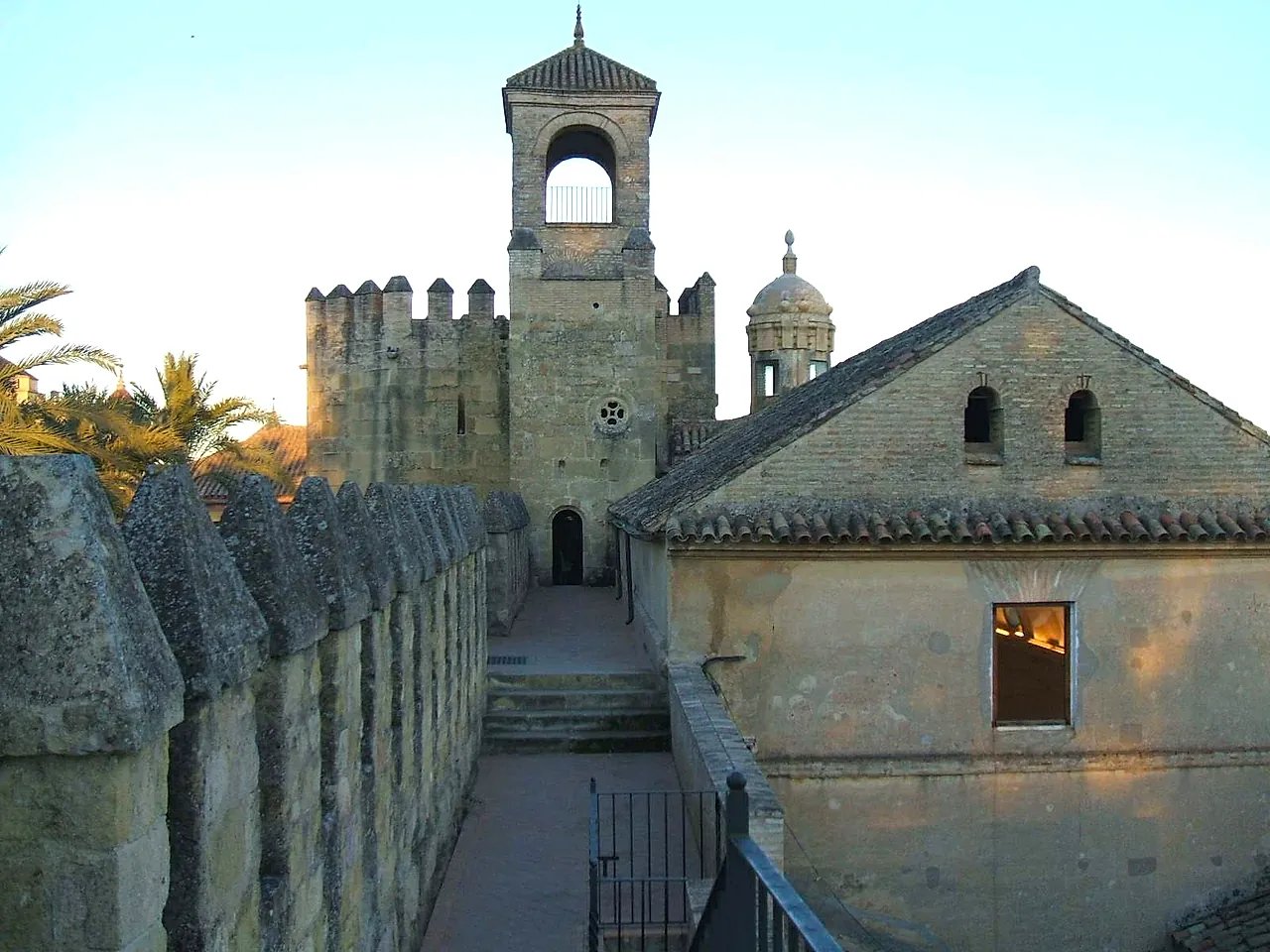 Crenellated battlements leading to a tower with a small belfry and a tiled roof at the Alcázar de los Reyes Cristianos