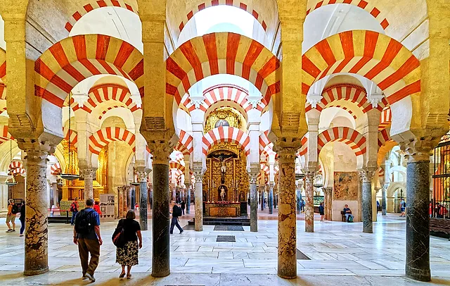 A long aisle of red-and-white arches inside the Mosque-Cathedral of Córdoba, with a lit chapel at the far end and visitors in the foreground